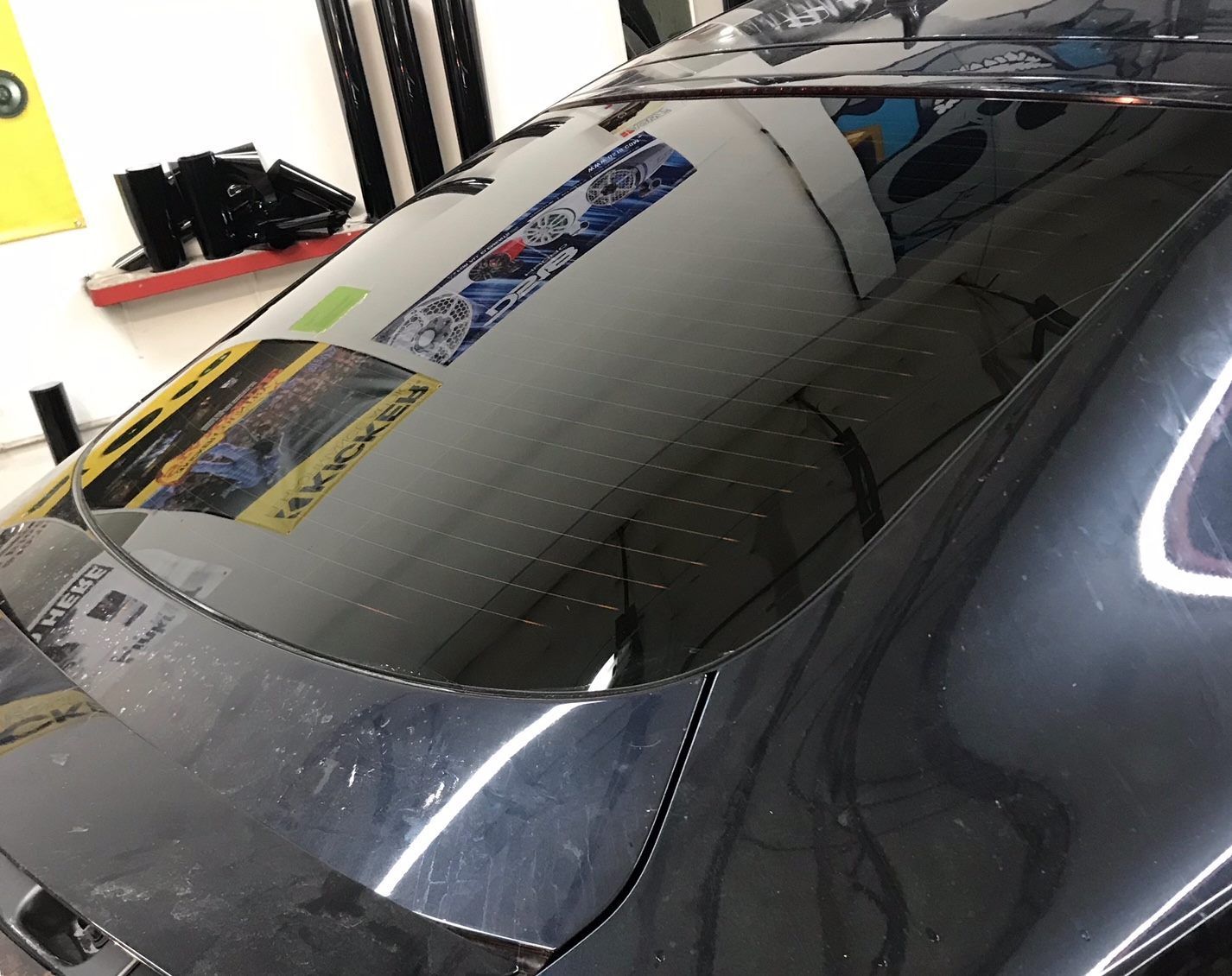 Black car with tinted rear window, reflecting the interior of a room.