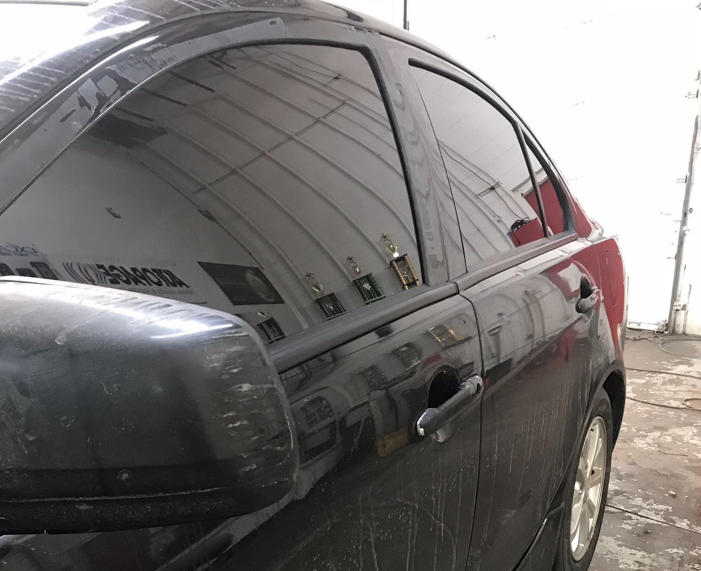 Black car with tinted windows and a side mirror. Reflects a garage.