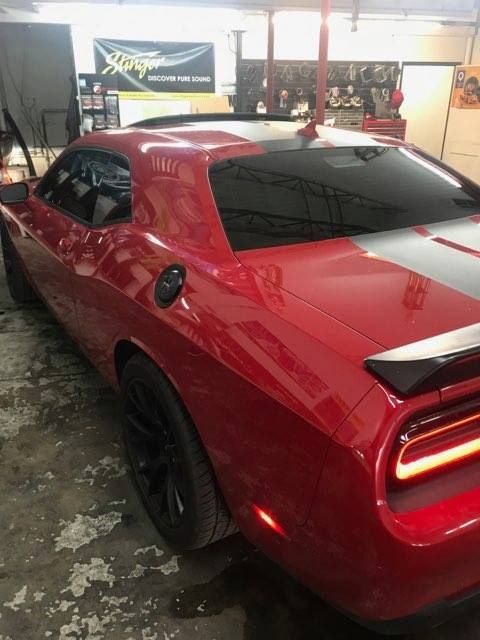 Red Dodge Challenger with black stripes, tinted windows, and black wheels inside a garage.