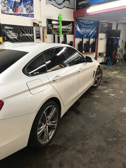 White BMW sedan with tinted windows parked inside a shop, wheels visible.
