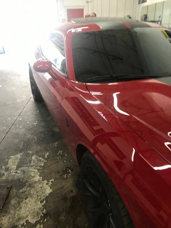 Red Dodge Challenger sports car with black tinted windows and a black stripe on the hood.