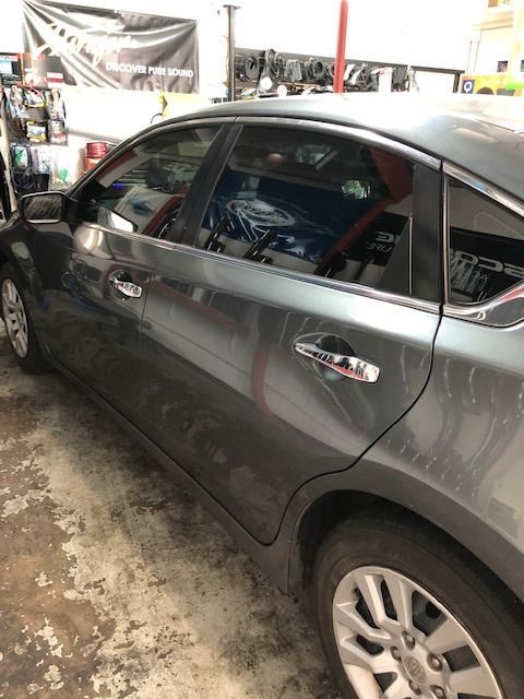 Gray Nissan Altima in a garage, tinted windows, silver door handles, dusty concrete floor.
