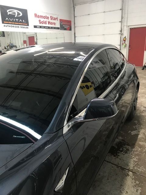 Dark gray Tesla car with tinted windows parked inside a garage.