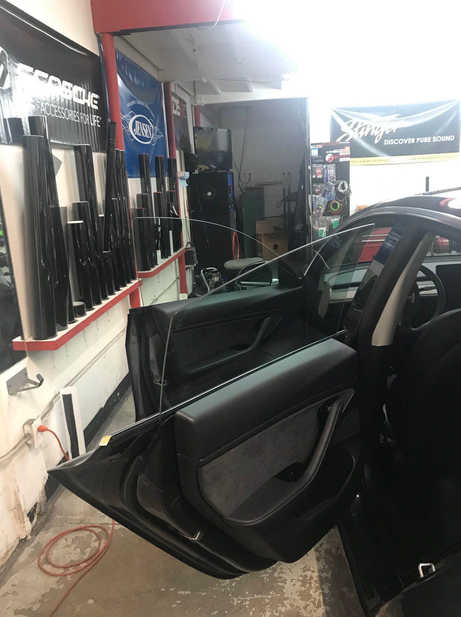 Black car door open inside a tint shop, rolls of window tint visible.