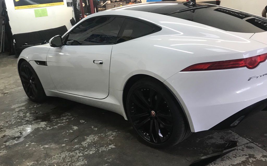 White Jaguar F-Type coupe with black wheels parked inside a garage, with tinted windows.