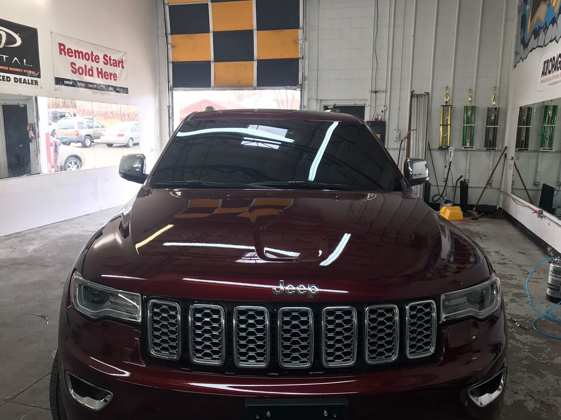 Dark red Jeep Grand Cherokee in a garage, tinted windows, with trophies in background.