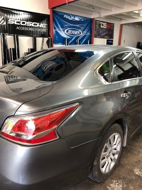 Gray sedan with tinted windows in a garage, tail light visible, background signs.