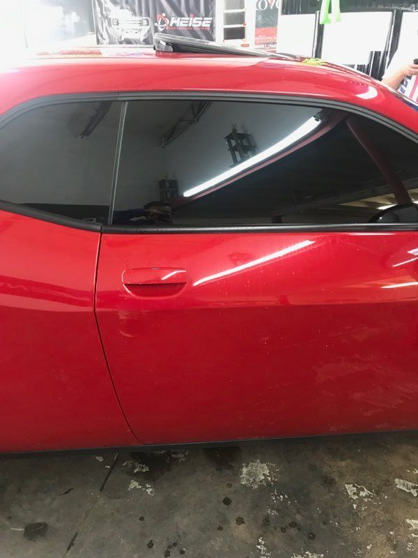 Red Dodge Challenger car with tinted windows in a shop.
