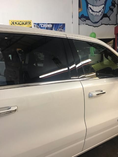 White car with tinted windows in a shop, displaying chrome door handles and trim.