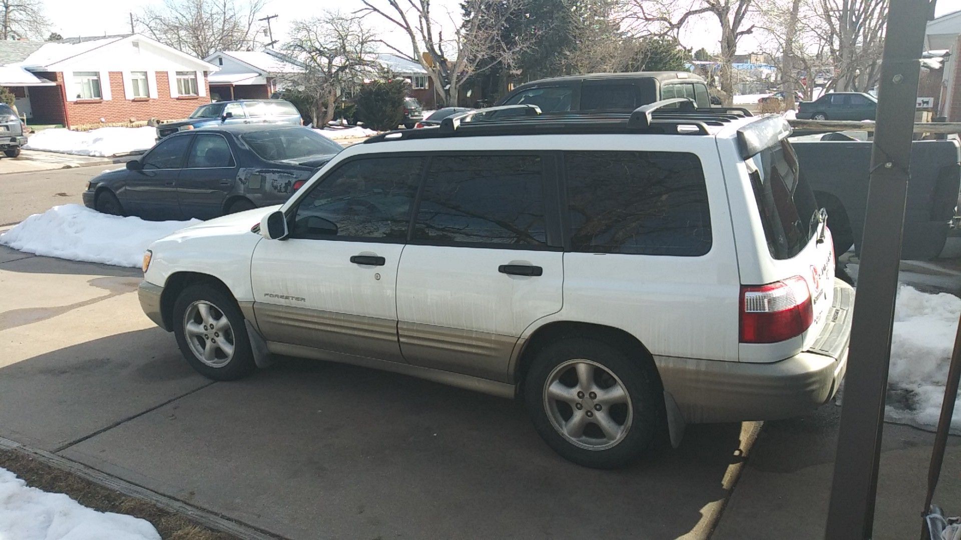 White SUV parked on a concrete driveway, with a dark car and snow in the background.
