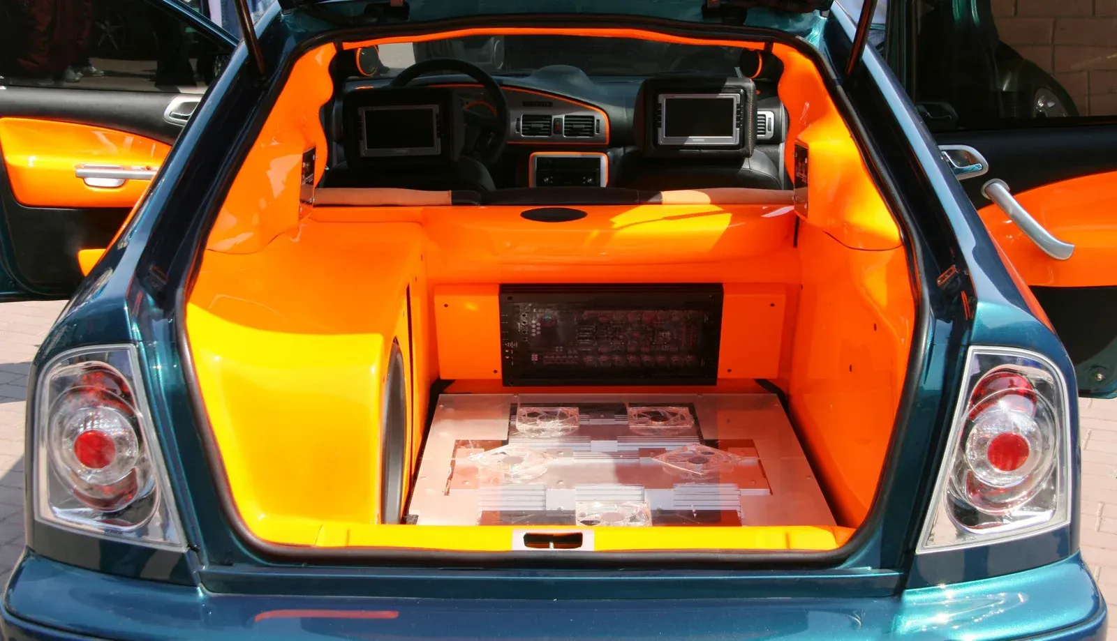 Green car trunk interior with bright orange accents, custom stereo, and multiple screens.