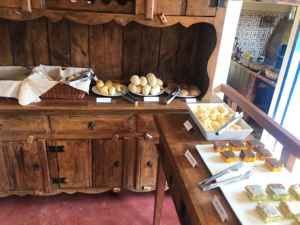 Buffet de madeira com pãezinhos, cubos de queijo e doces.