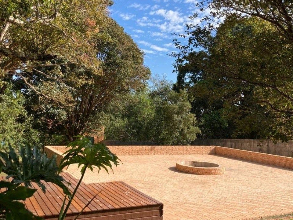 Pátio em terraços com lareira circular, rodeado por árvores exuberantes sob um céu azul.