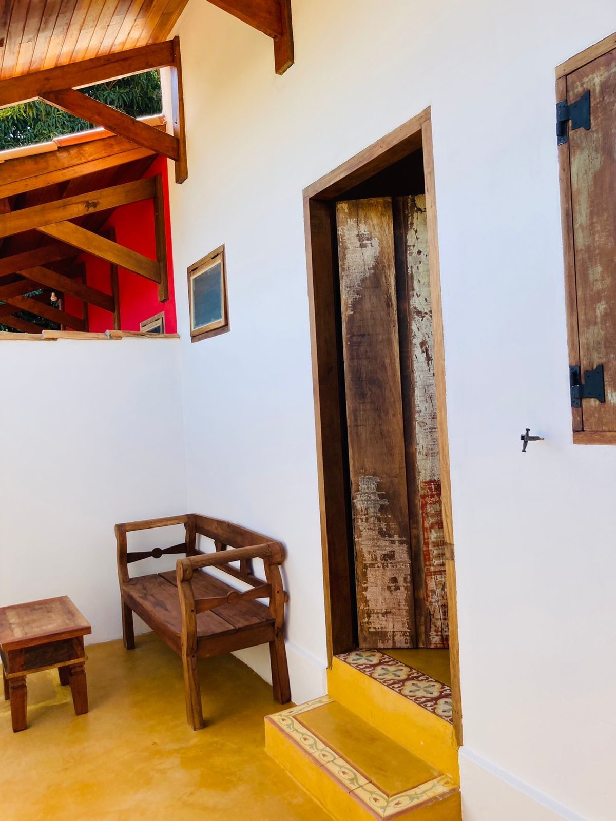 Interior com banco de madeira e porta que dá acesso à escada; parede com destaque em vermelho.