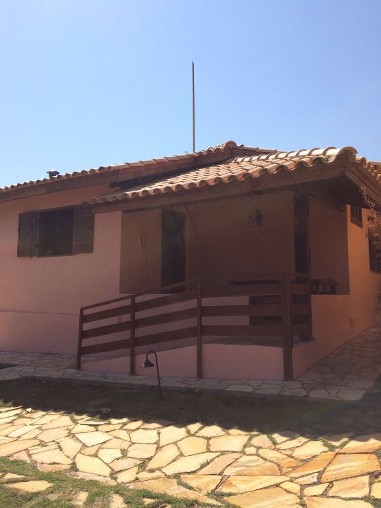 Casa rosa com telhado marrom, varanda de madeira e caminho de pedra.