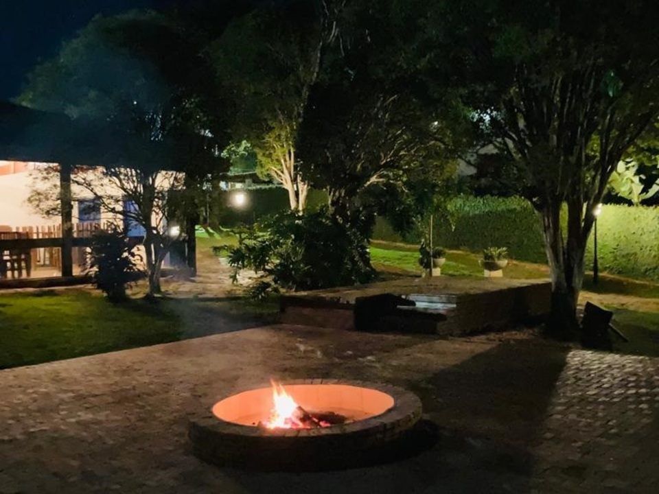 Fogueira com chamas à noite em um quintal com gazebo e árvores.
