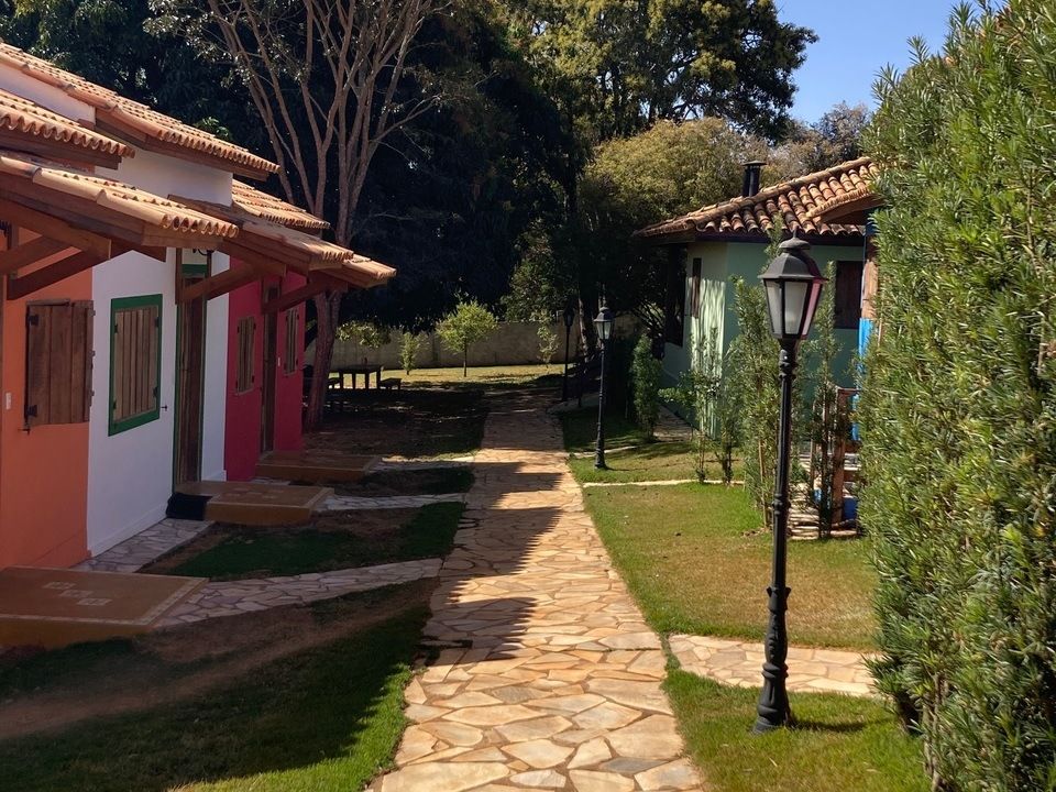 Caminho de pedra entre edifícios coloridos, vegetação exuberante e postes de luz, em um dia ensolarado.