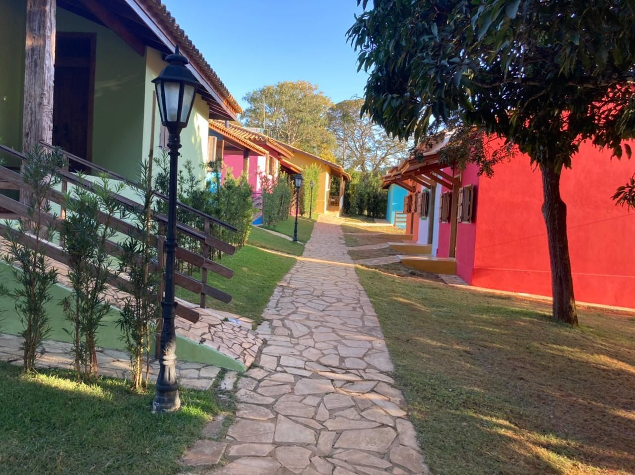 Caminho de pedra entre edifícios coloridos com paredes vermelhas, rosas, verdes e azuis; um ambiente externo ensolarado.