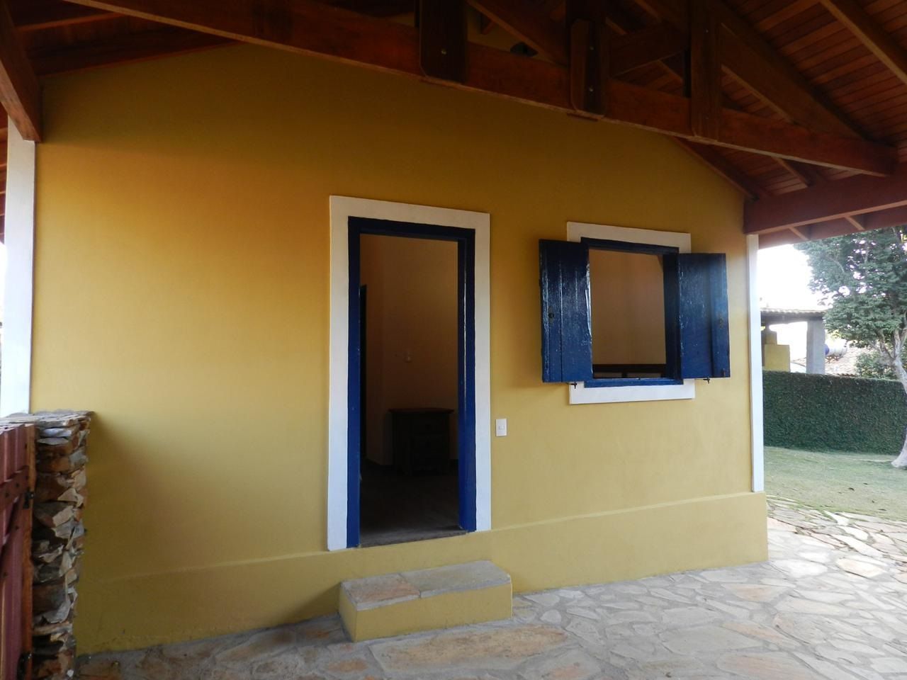 Prédio amarelo com porta e janelas venezianas azuis, detalhes brancos e uma varanda.