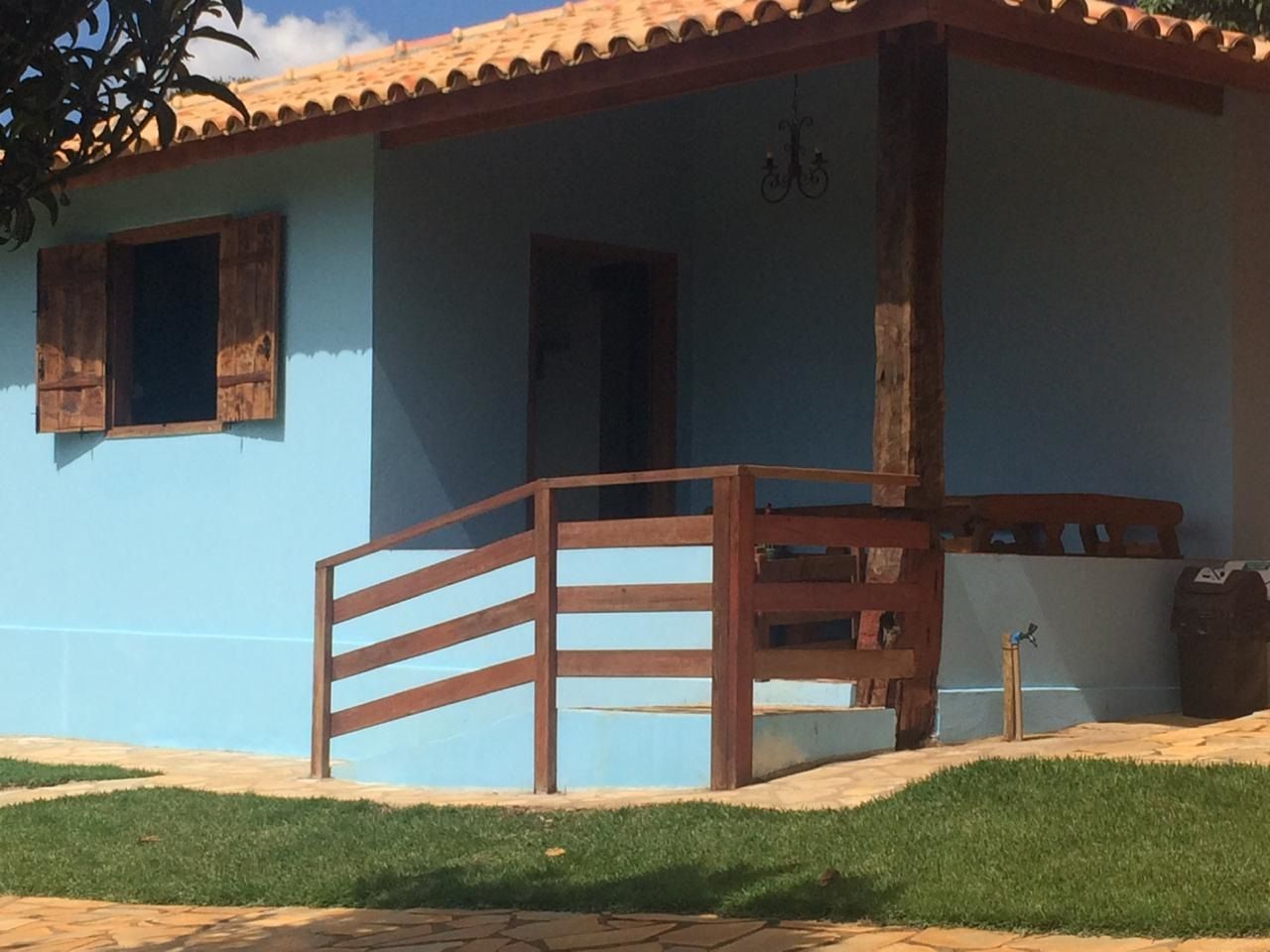 Casa azul com detalhes e grades marrons, sob um telhado de telhas de terracota, com grama verde na frente.