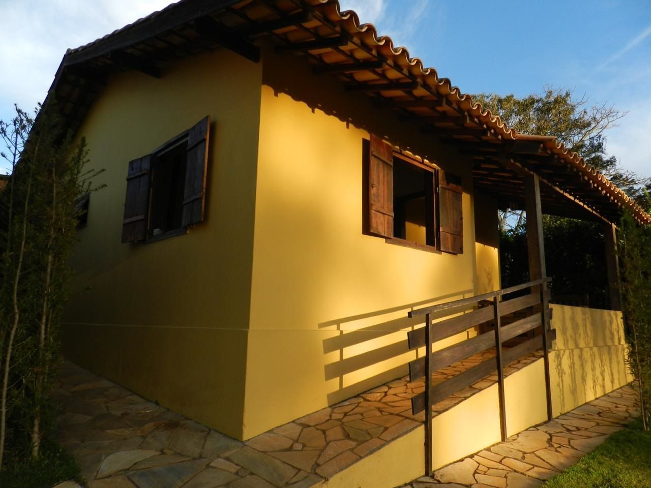 Casa amarela de estuque com persianas marrons, telhado de telha e rampa de acesso.