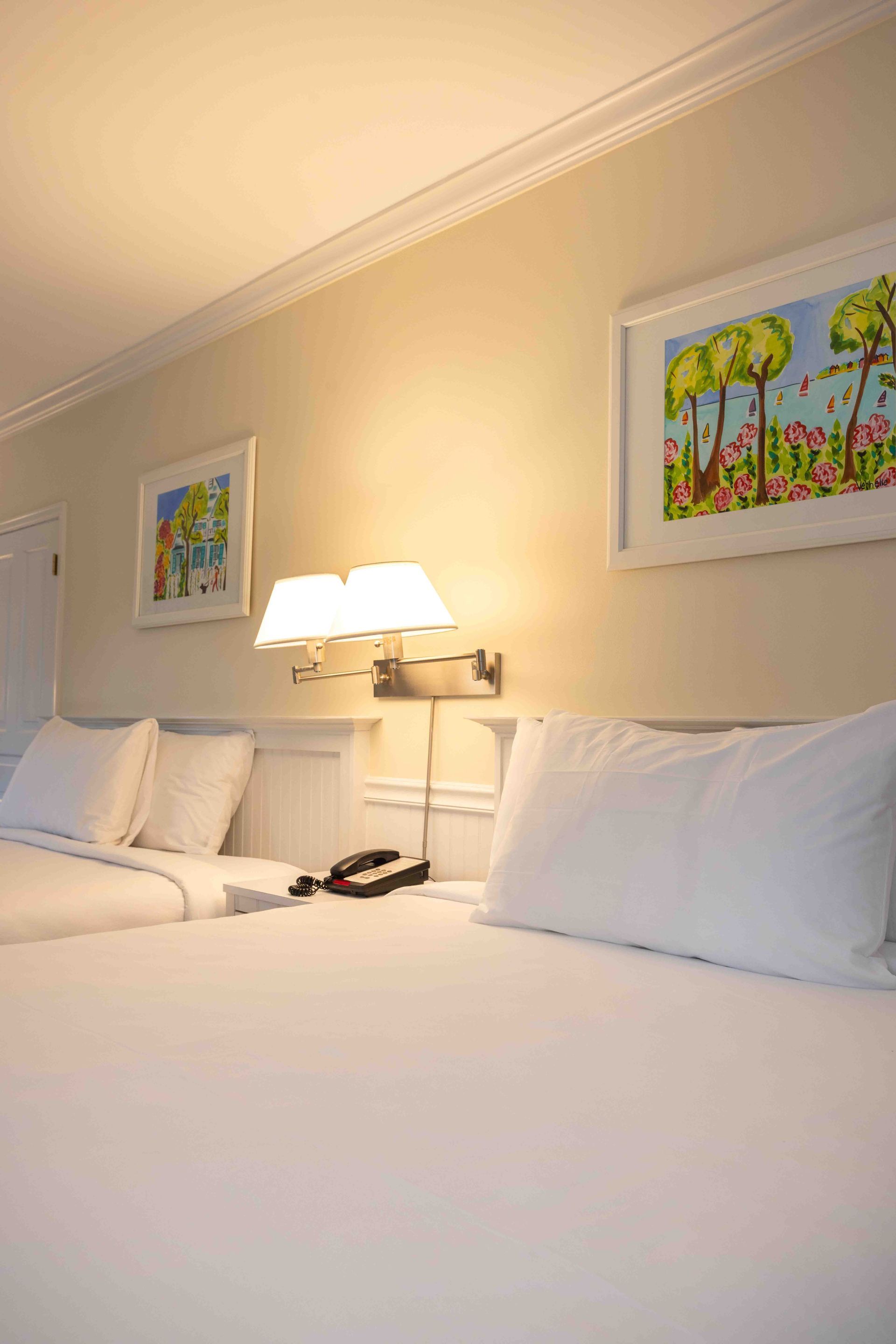 A hotel room with two beds , two lamps and two pictures on the wall.