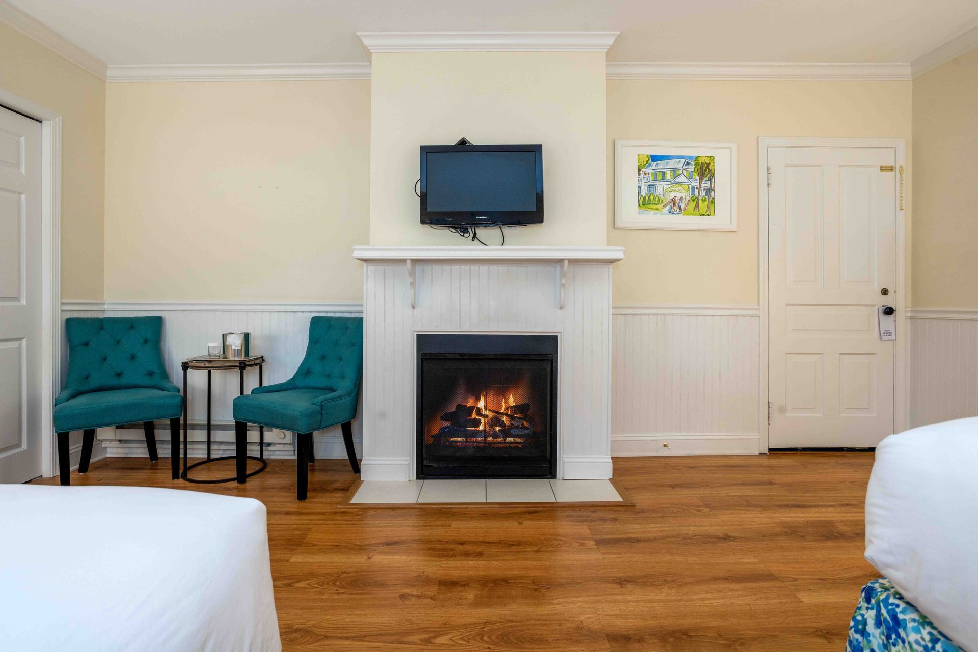 A hotel room with two beds , chairs , a fireplace and a flat screen tv.
