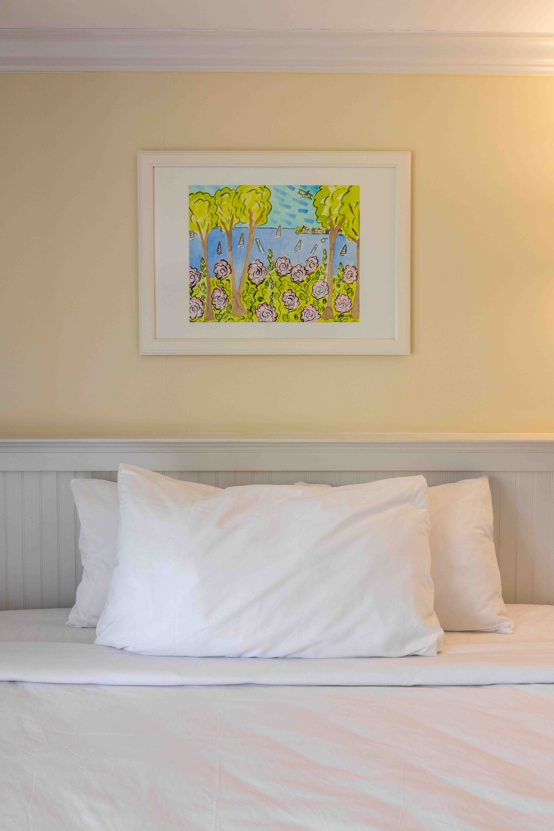 A bed with white sheets and pillows and a picture on the wall above it.