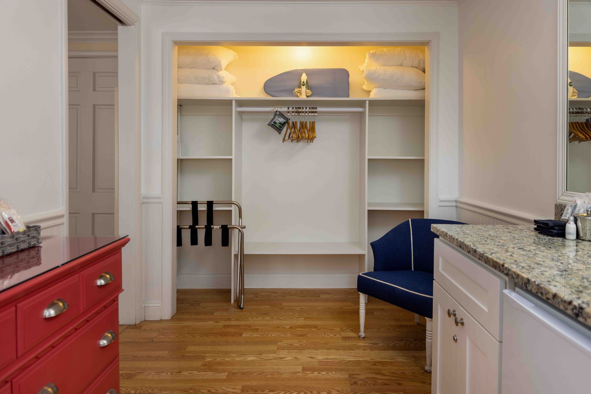 A hotel room with a dresser , chair , sink and closet.