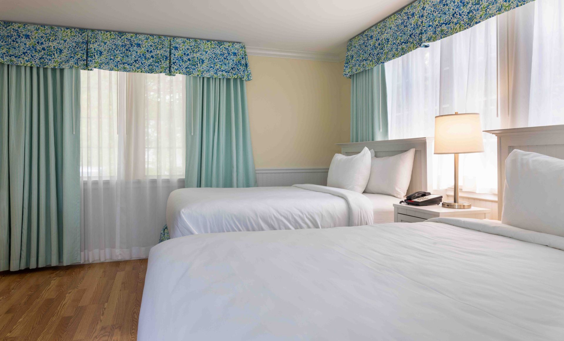 A hotel room with two beds and two windows.