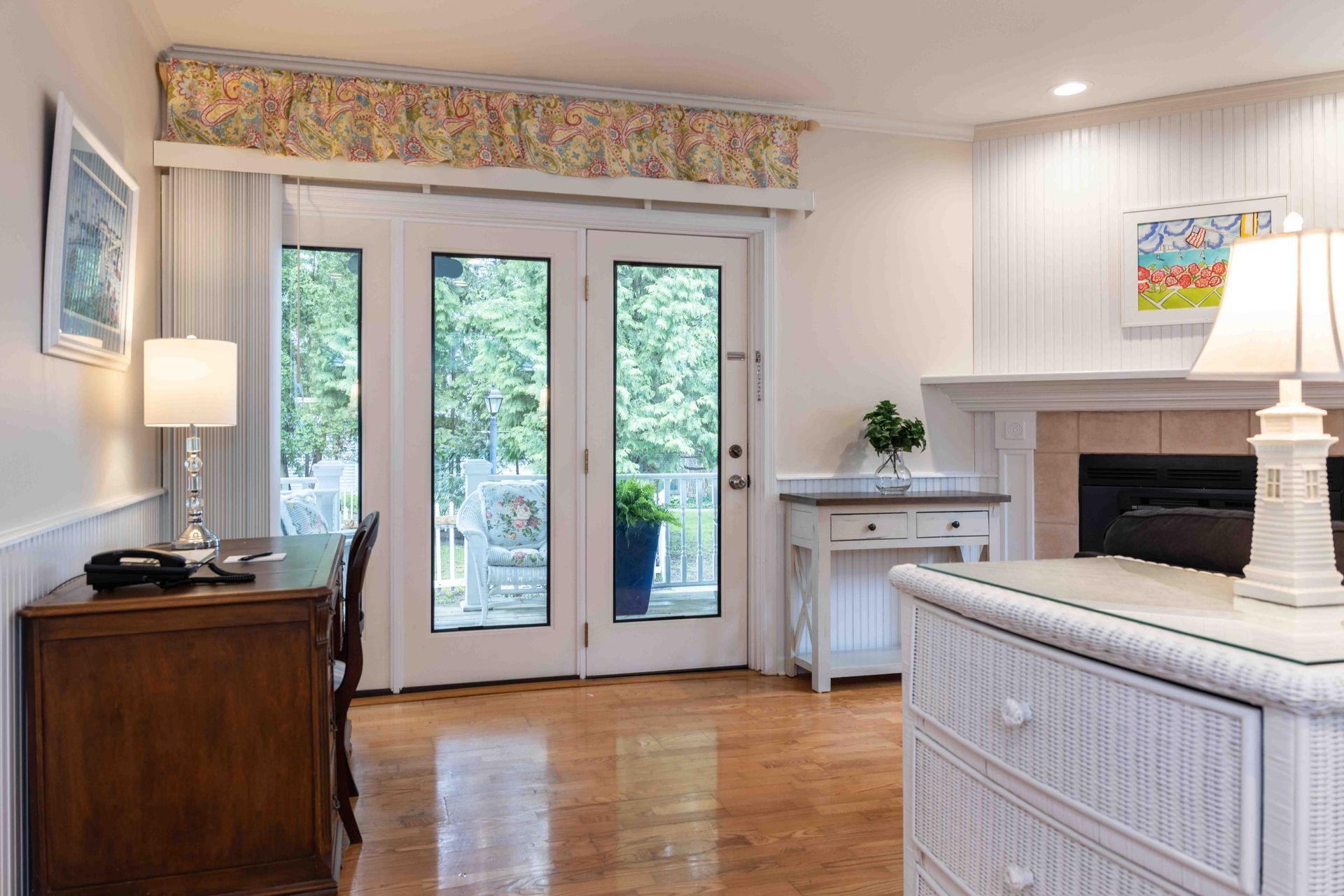 A living room with hardwood floors , a desk , dresser and fireplace.