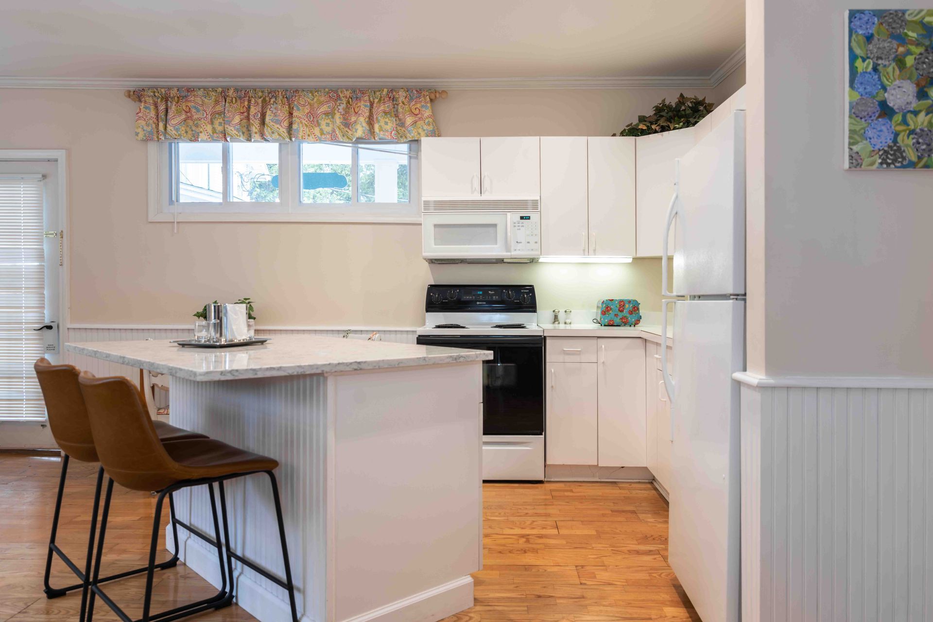 A kitchen with white cabinets , a stove , a refrigerator , and a bar.