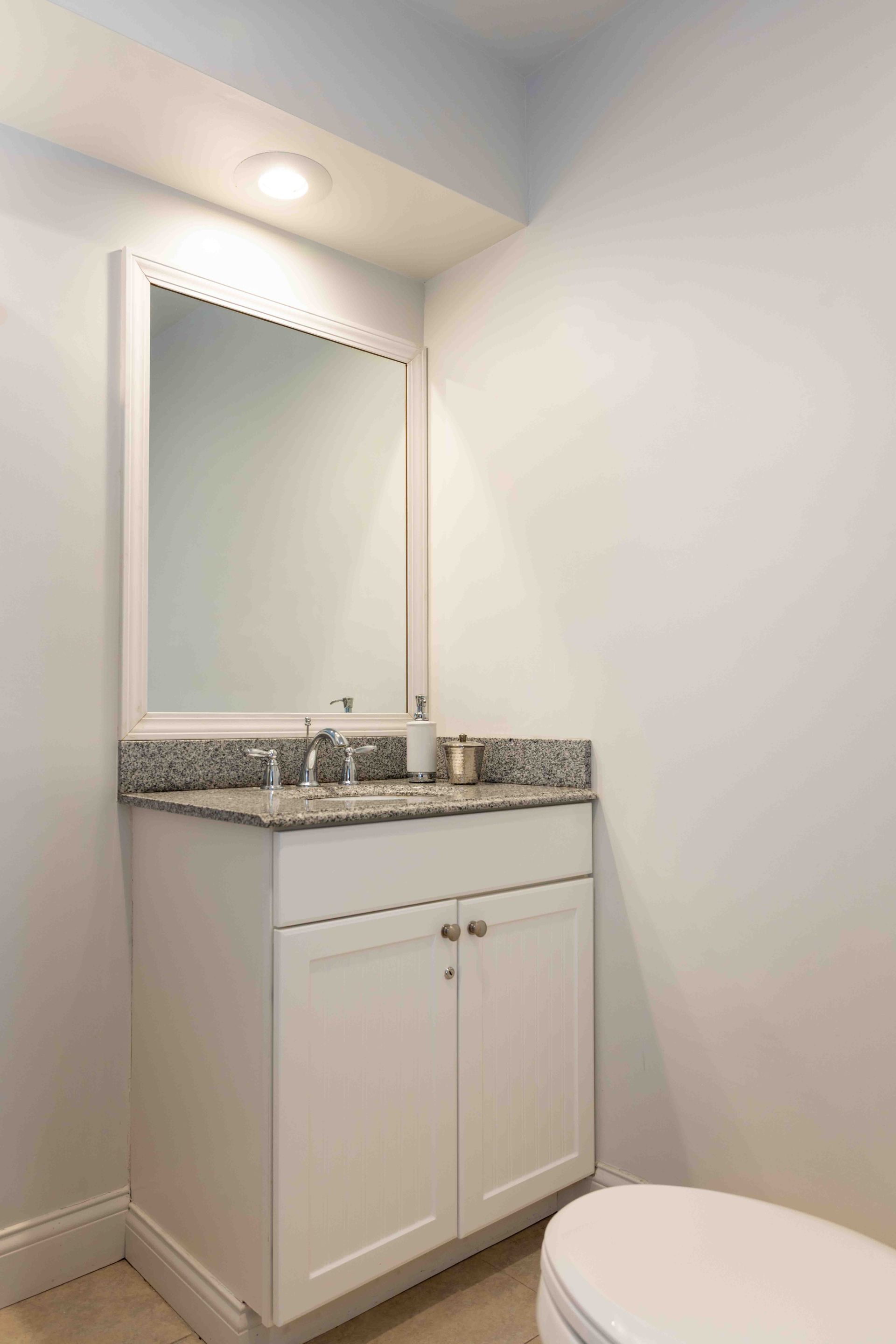 A bathroom with a sink , toilet , mirror and vanity.