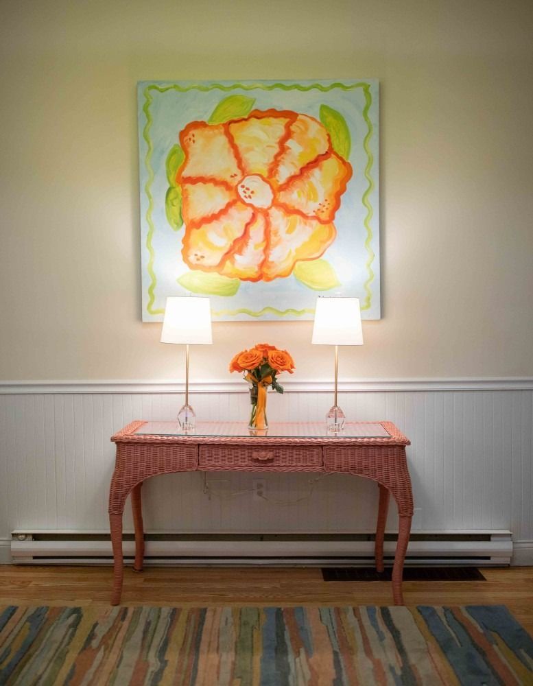 There is a painting of a flower on the wall above a table.