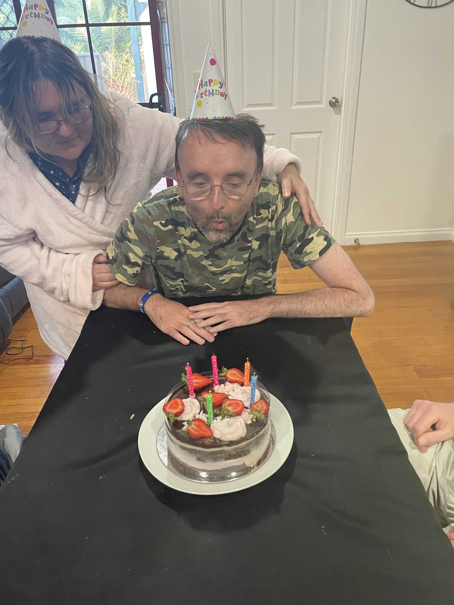 A Man is Sitting at a Table With a Birthday Cake and Candles — Keilor East, VIC — North West Melbourne Family Respite