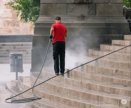 Person in red shirt power washes stone stairs, creating steam.
