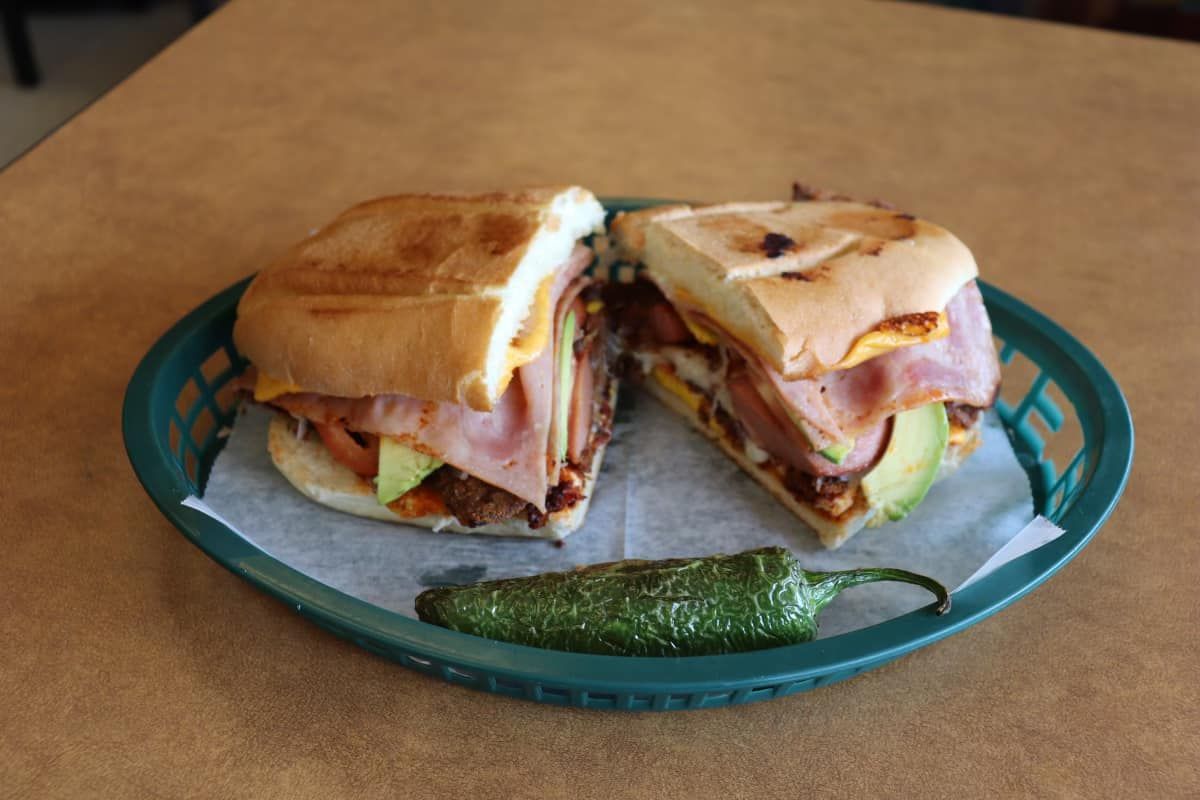 A sandwich in a basket with a green pepper next to it.