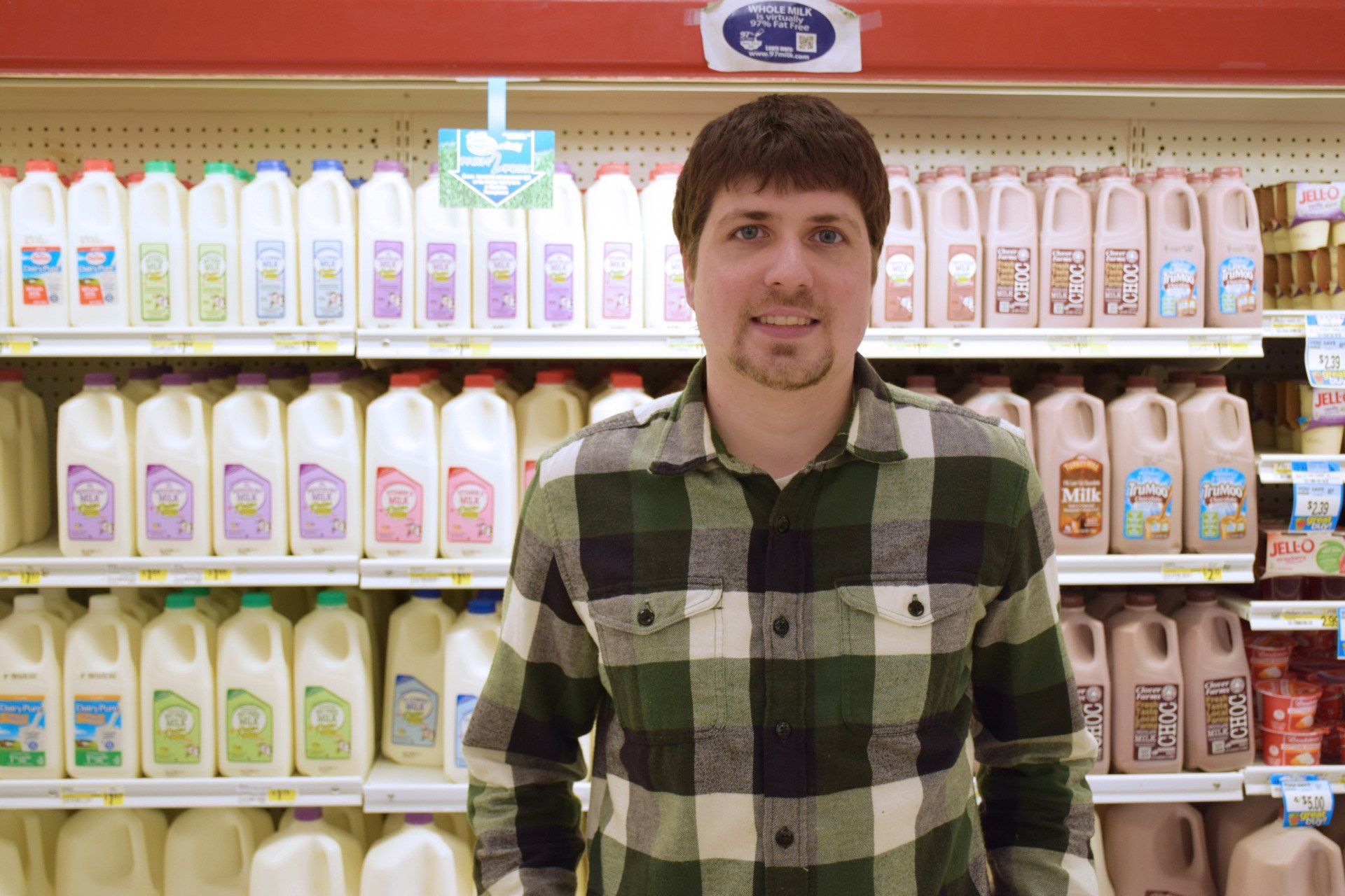 A man is standing in front of a shelf of milk in a grocery store.
