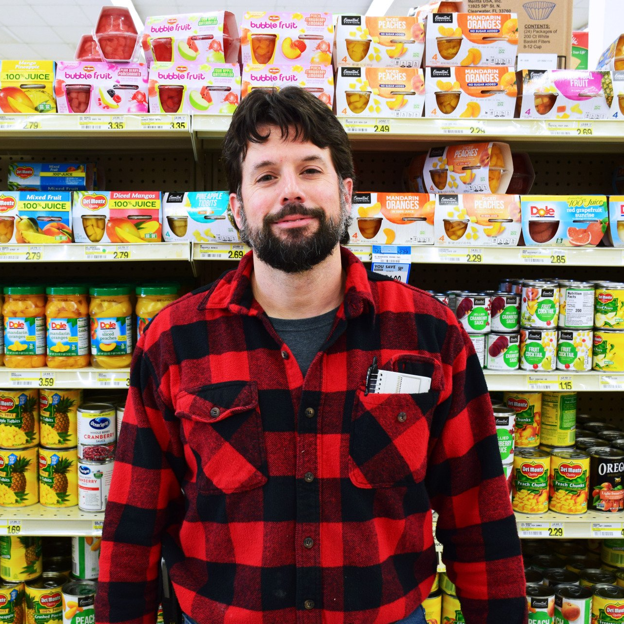A man in a red and black plaid shirt is standing in front of a grocery shelf