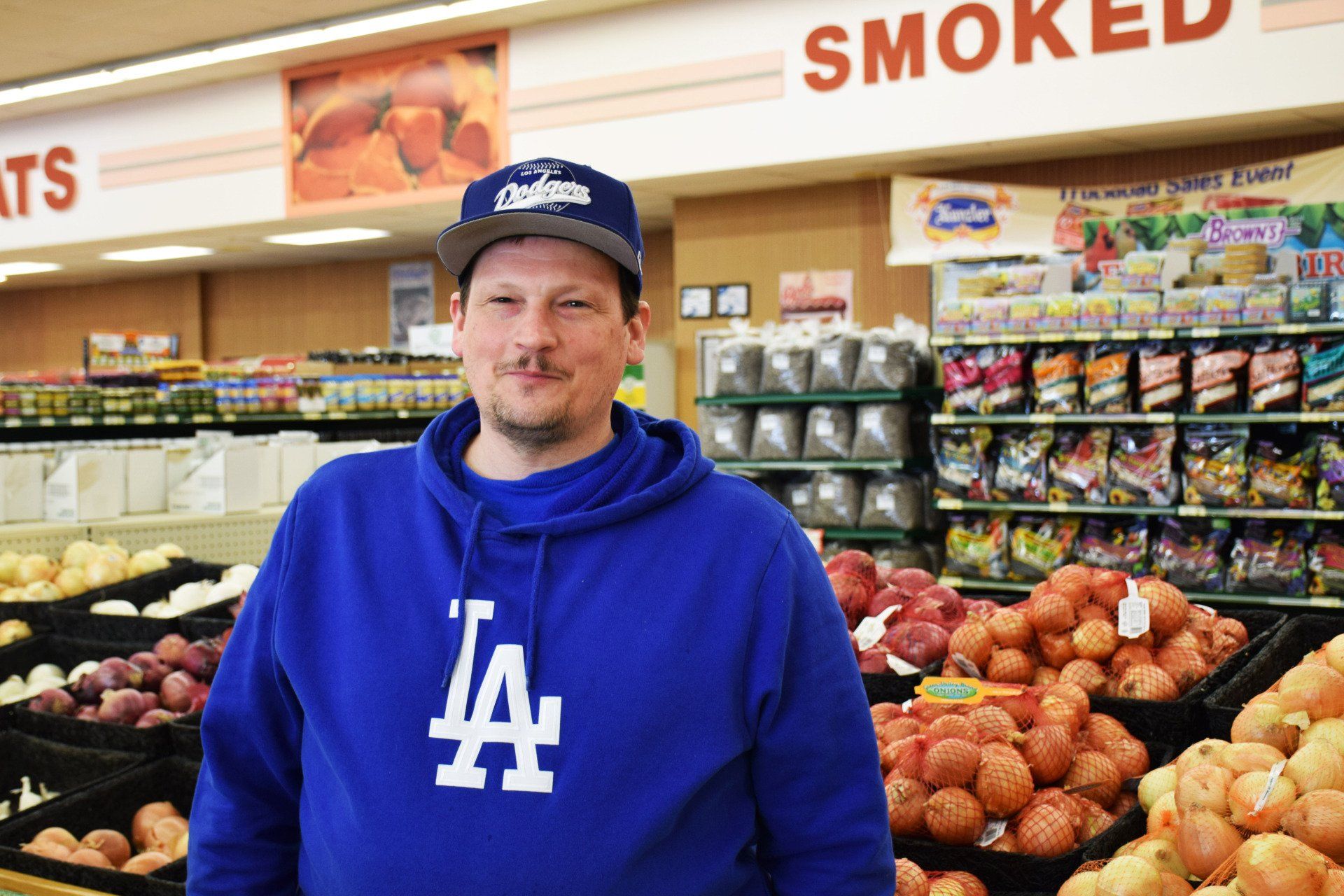 A man wearing a la dodgers sweatshirt is standing in a grocery store.