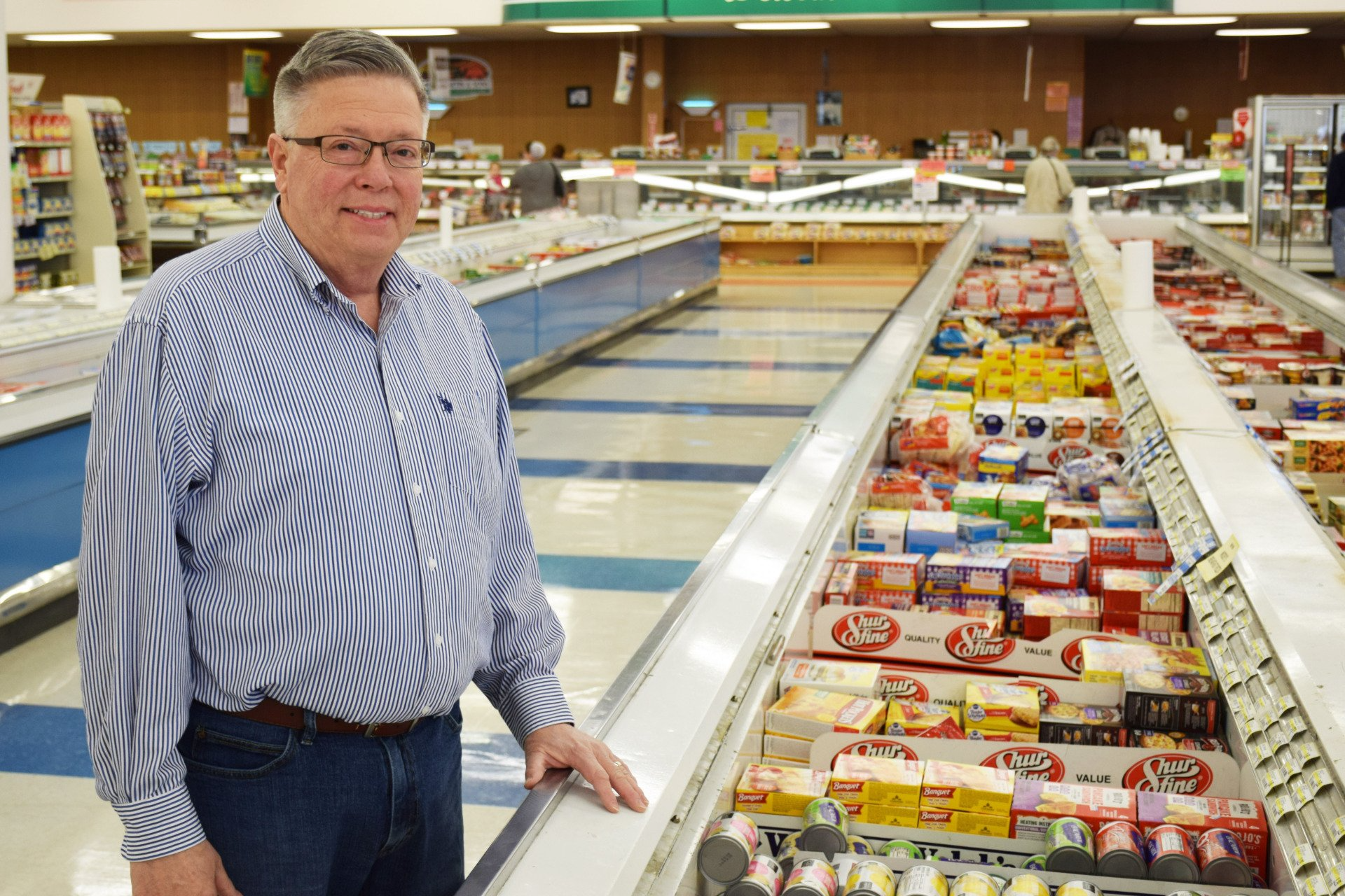 A man is standing in front of a refrigerator in a grocery store.