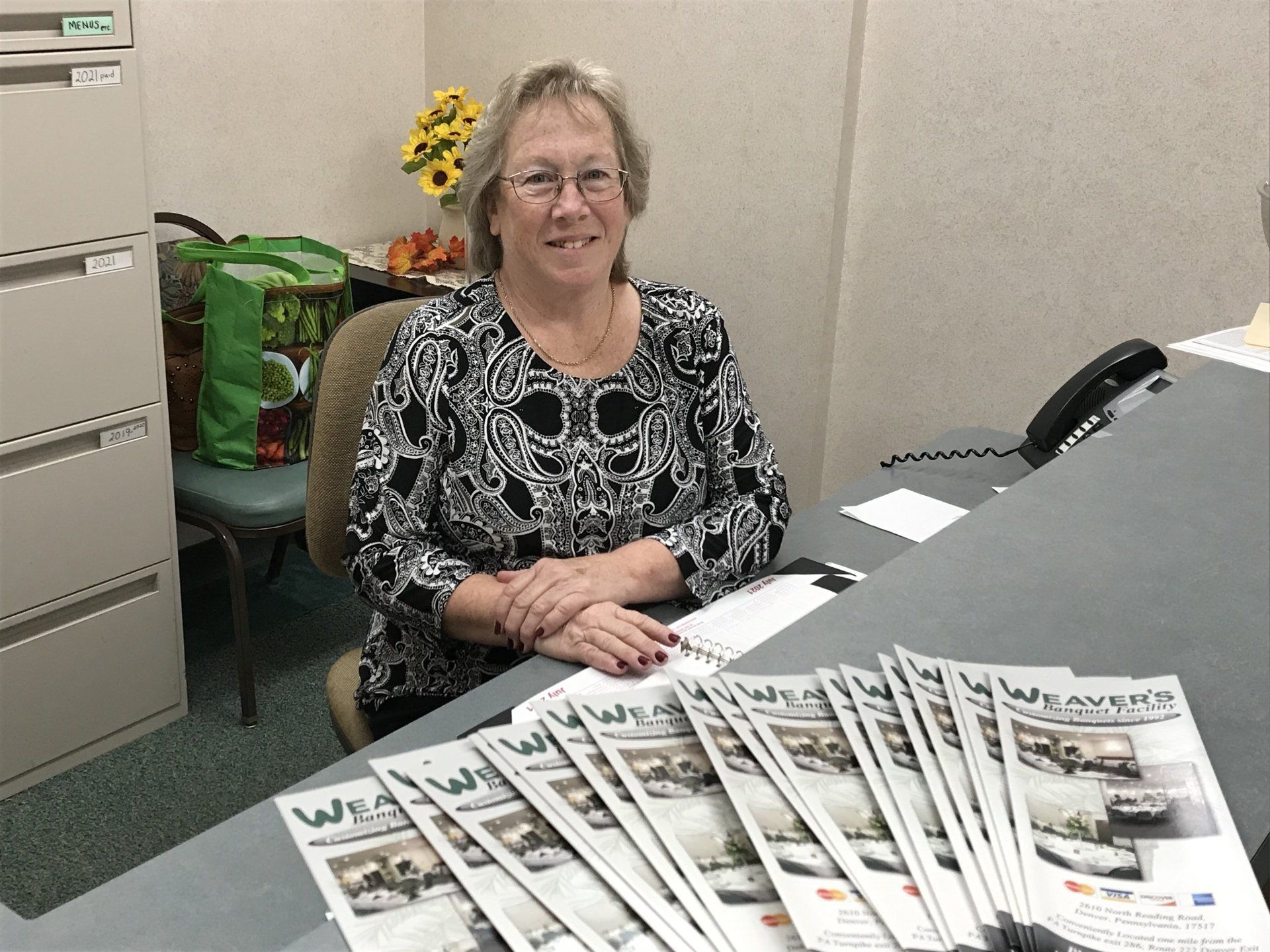 A woman is sitting at a desk with a bunch of newspapers on it.