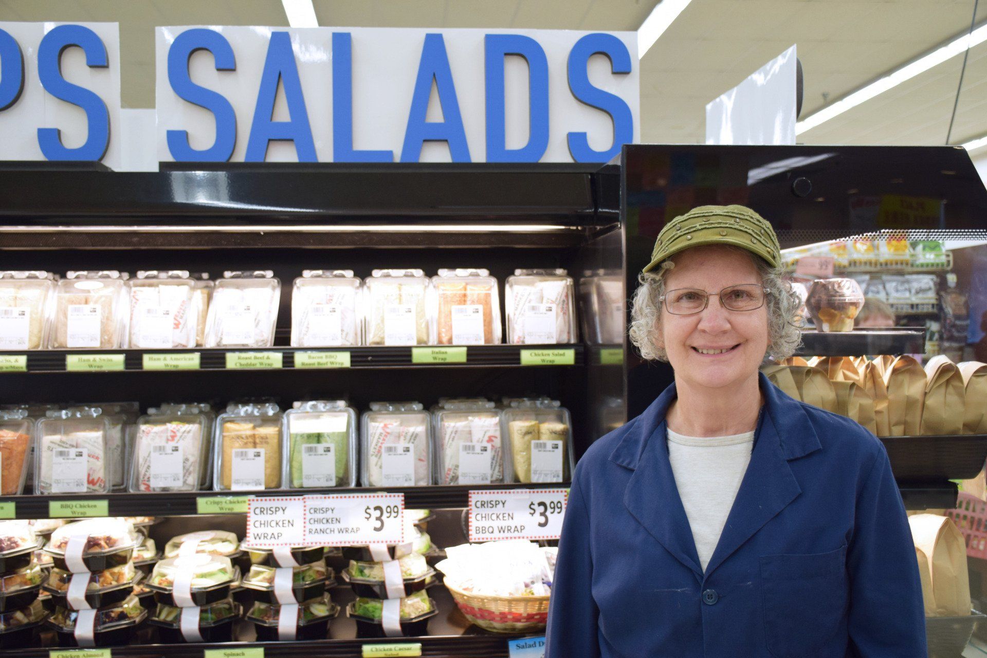 A woman is standing in front of a salad display in a grocery store.