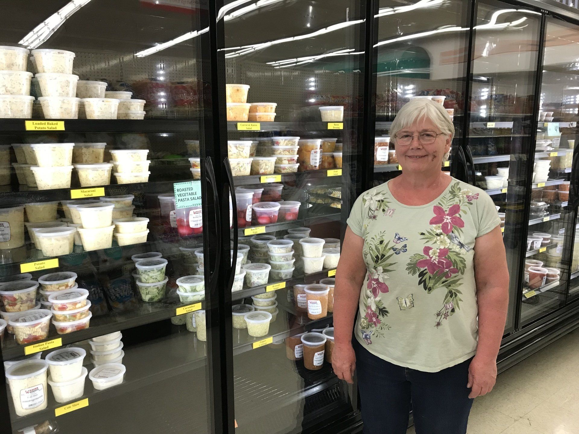 A woman is standing in front of a refrigerator in a grocery store.