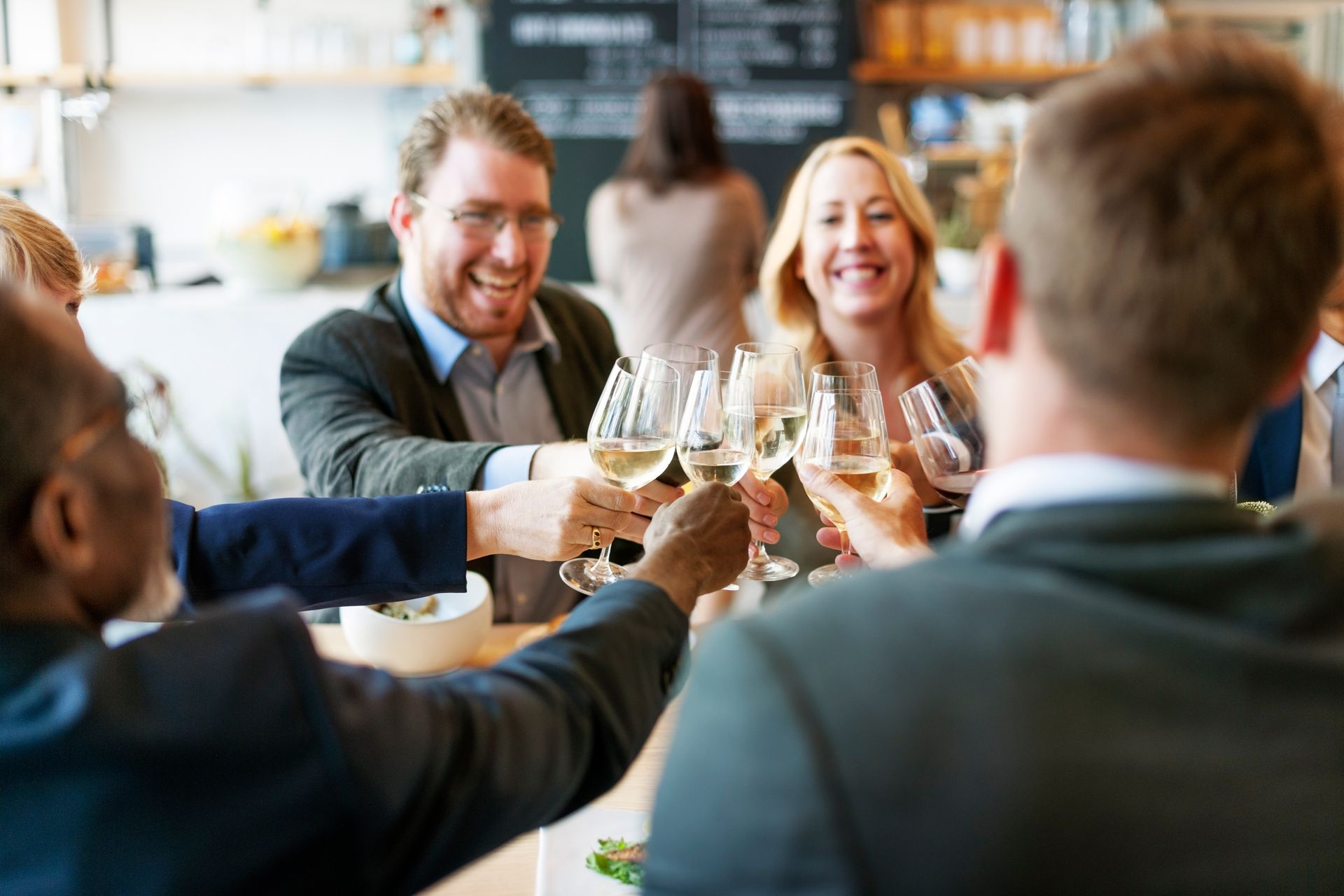 A group of people in business attire toast with glasses of white wine at a restaurant table.