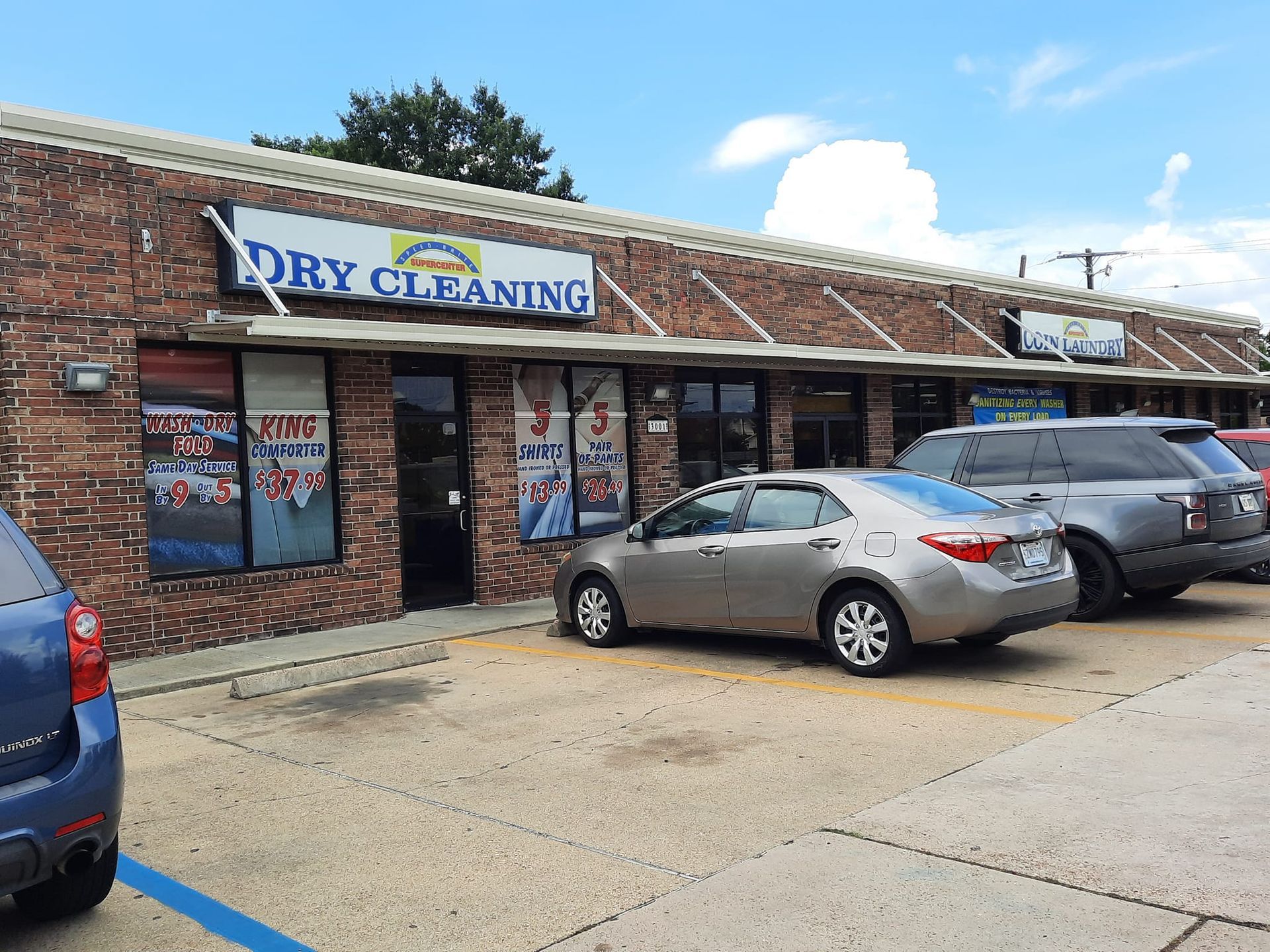 Dry cleaning business storefront with signage, parked cars, and a blue sky.