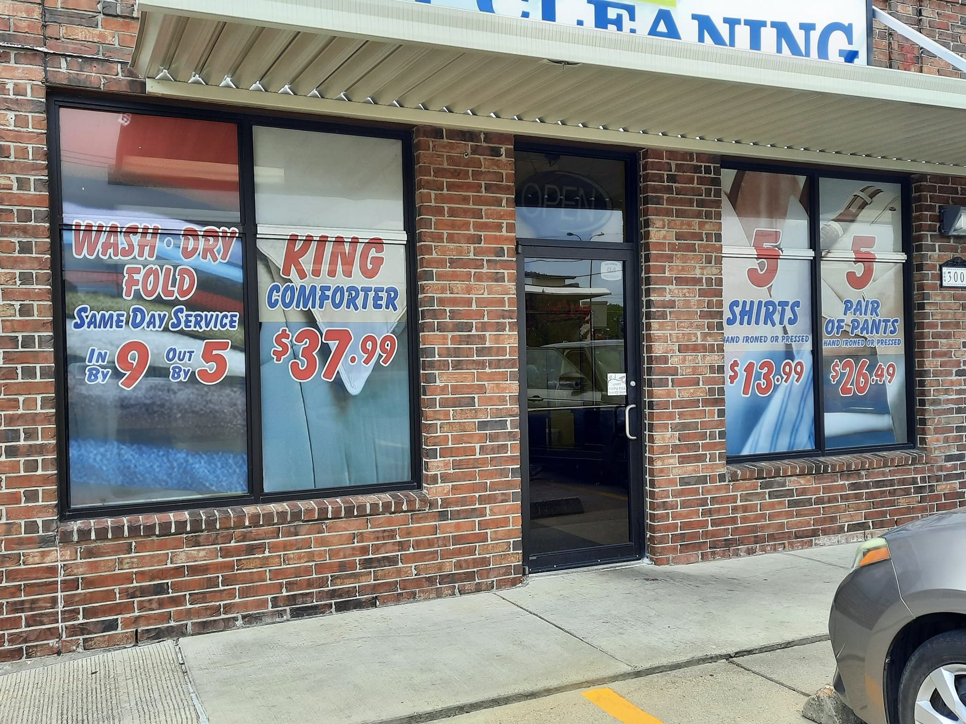 Exterior of a brick dry cleaning business with promotional window signs; door is open.