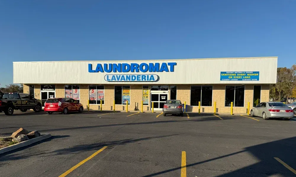 Laundromat building with blue signage, cars parked in front. Sunny day.