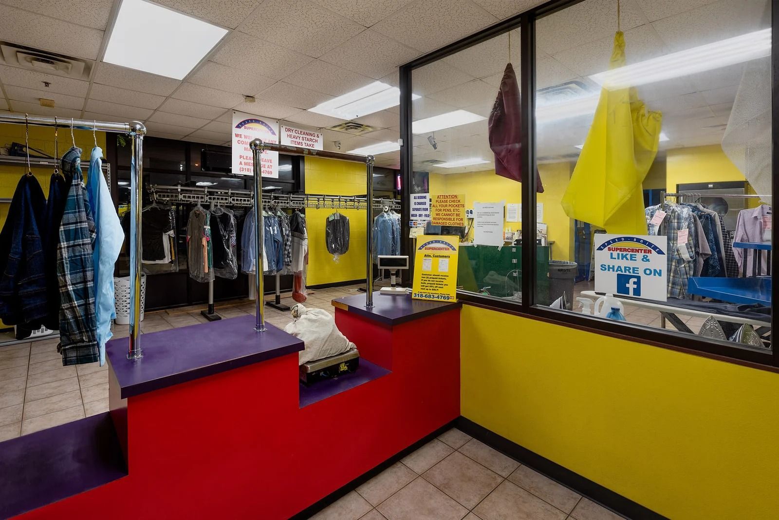 Interior of a dry cleaner, featuring racks of clothes, a counter, and yellow and red walls.