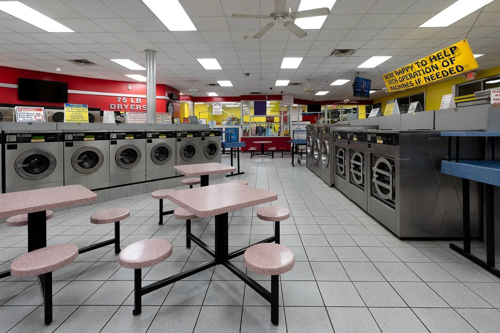 Interior of a laundromat with rows of washers and dryers, tables, and seating.